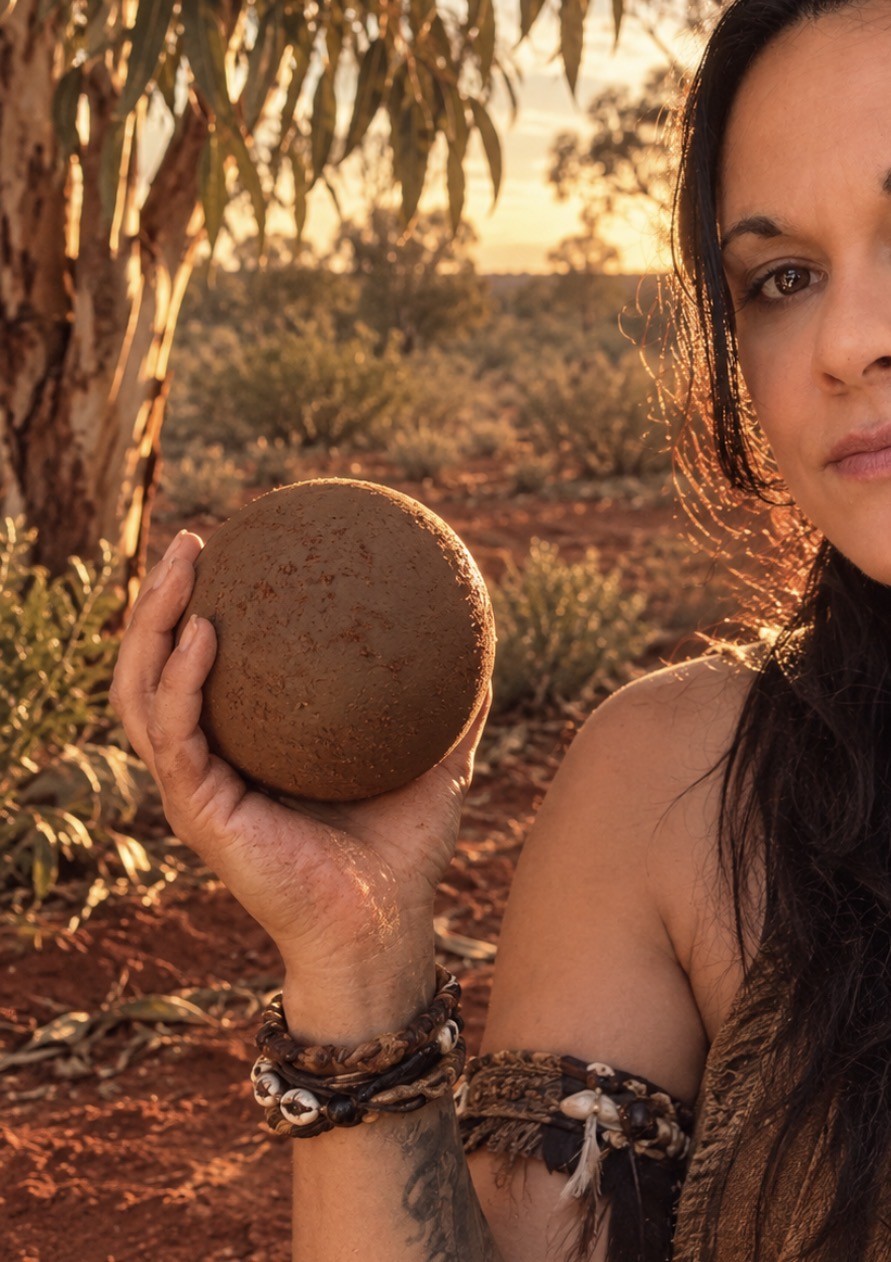 Yoorana holding a handmade earth piece outdoors at sunset