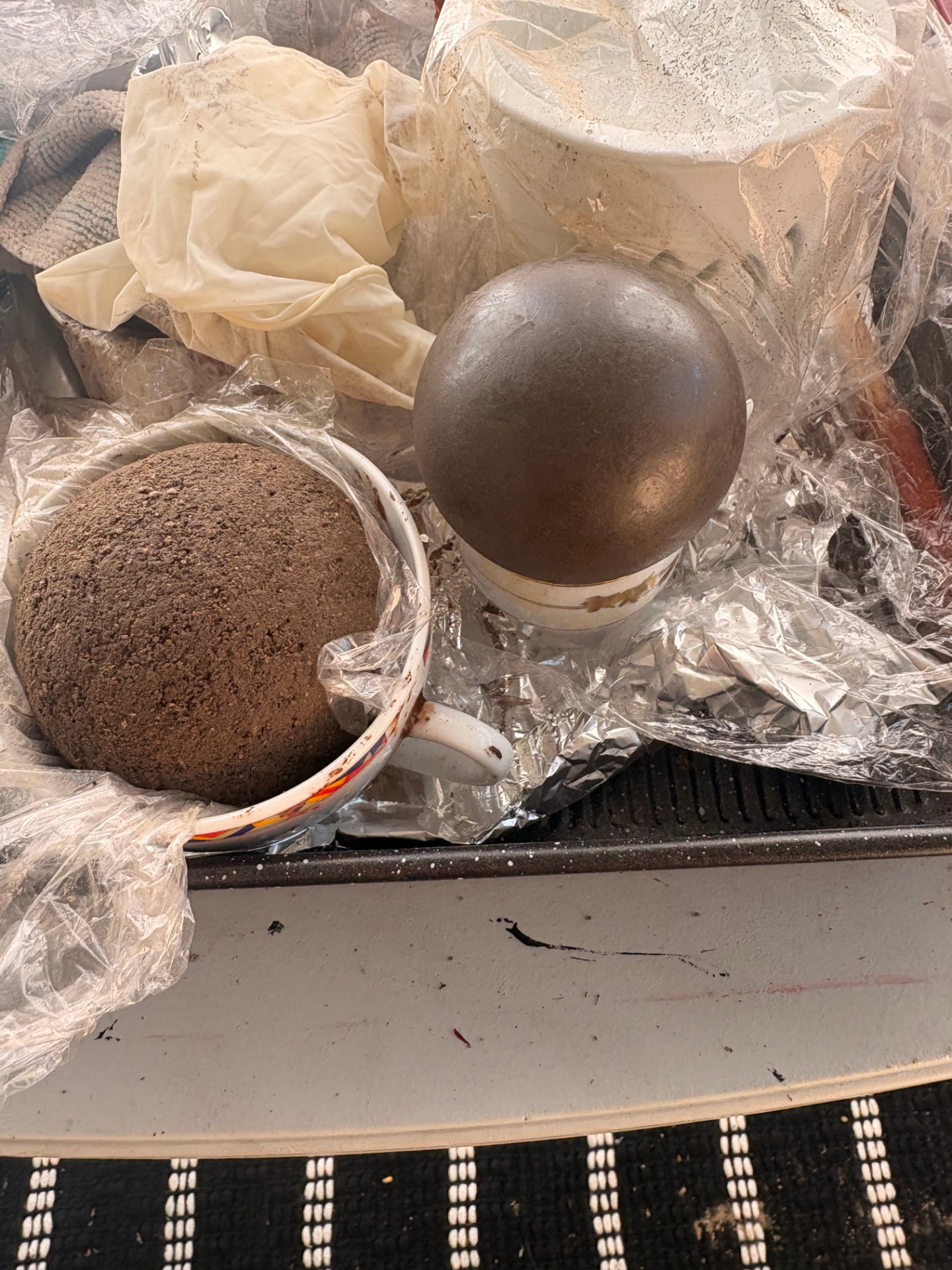 A rough earth piece in a cup beside a polished Dhawun Buru on a stand